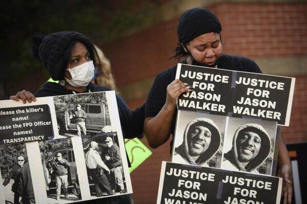 FILE - Pandora Harrington, right, cries as she holds a sign with an image of Jason Walker during a demonstration in front of the Fayetteville Police Department, Jan. 9, 2022, in Fayetteville, N.C.  An autopsy released Thursday, March 24, 2022, by North Carolina’s Office of the Chief Medical Examiner said that 37-year-old pedestrian Jason Walker had wounds to his head, chest, back and thigh in the Jan. 8 shooting. The deputy has said he was defending himself after Walker jumped on the hood of his truck. The shooting prompted protests by demonstrators who questioned authorities’ account of what happened.  (Andrew Craft/The Fayetteville Observer via AP)