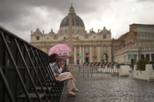 A woman shelters against the rain outside St. Peter's Basilica, background, in Rome, on Wednesday, May 7, 2025, on the day cardinals sequester themselves at the Vatican for the start of a conclave to elect the 267th Roman pontiff, a successor to Pope Francis. (AP Photo/Francisco Seco)