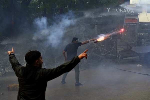 A protester launches fireworks at riot police during a demonstration in solidarity with the Palestinian people in Gaza, near the U.S. embassy in Aukar, a northern suburb of Beirut, Lebanon, Wednesday, Oct. 18, 2023. (AP Photo/Bilal Hussein)