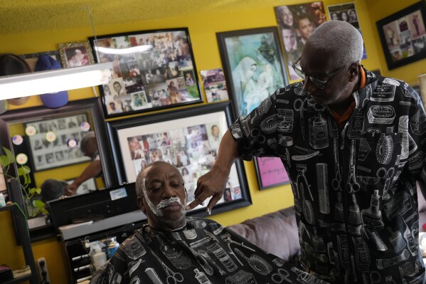 Barber Glenn Paige, right, who grew up in neighboring Winter Park, Fla. and chose to open his business in Eatonville, rubs shaving cream onto client Pastor Walter Harris, Thursday, Aug. 24, 2023, as he prepares him for a shave at Blessed by the Best barbershop in Eatonville, Fla. Paige treasures Eatonville's unique history as a self-governing Black municipality, and preserved two bricks from the now demolished Robert Hungerford Normal and Industrial School which he plans to decorate with the school's name and dates of operation and display in his shop. (AP Photo/Rebecca Blackwell)