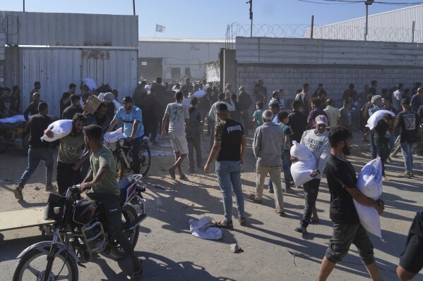 Palestinians carry bags of flour after storming a U.N. World Food Program warehouse in Zawaida, Central Gaza Strip, on Wednesday, May 28, 2025. (AP Photo/Abdel Kareem Hana)