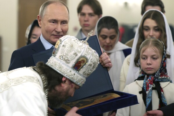 Russian Orthodox Archbishop of Odintsovo and Krasnogorsk Foma (Nikolay Mosolov), foreground, kisses an icon as Russian President Vladimir Putin, left, stands near after attending an Orthodox Christmas service with the families of military personnel who died during the special military operation in Ukraine in the Church of Our Savior Not Made by Hands at the Novo-Ogaryovo state residence outside Moscow, Russia, on Sunday, Jan. 7, 2024. (Gavriil Grigorov, Sputnik, Kremlin Pool Photo via AP)