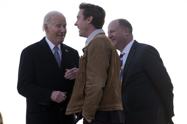 El presidente Joe Biden saluda al gobernador de Colorado, Jared Polis, a la derecha, y al alcalde de Denver, Mike Johnston, cuando llega en el Air Force One al Aeropuerto Internacional de Denver, el martes 28 de noviembre de 2023, en Denver.  (Foto AP/Andrew Harnik)