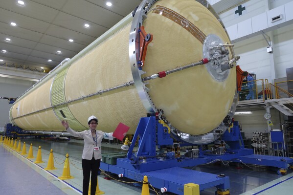 FILE - A Mitsubishi Heavy Industries staff member stands next to the top of the first stage of a H3 rocket, inside the Mitsubishi Heavy Industries' Nagoya Aerospace Systems Works Tobishima Plant in Tobishima, Aichi prefecture Thursday, March 21, 2024. Japan’s space agency announced Friday, April 26, that it will launch its new flagship rocket H3 on June 30 carrying an observation satellite for disaster response and security purposes, a key mission that it had failed in its debut flight last year.(AP Photo/Mari Yamaguchi)