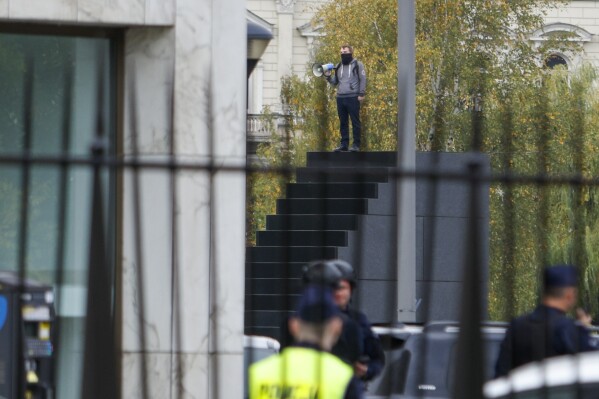 A man who has allegedly threatened to blow himself up stands on a monument in Warsaw, Poland, Saturday, Oct. 14, 2023. Large numbers of police and special counter-terror officers sealed off a large square in the Polish capital on Saturday after a man who climbed to the top of a monument threatened to blow himself up, the Polish news agency PAP reported. The incident came on the eve of a critical election. (AP Photo/Michal Dyjuk)