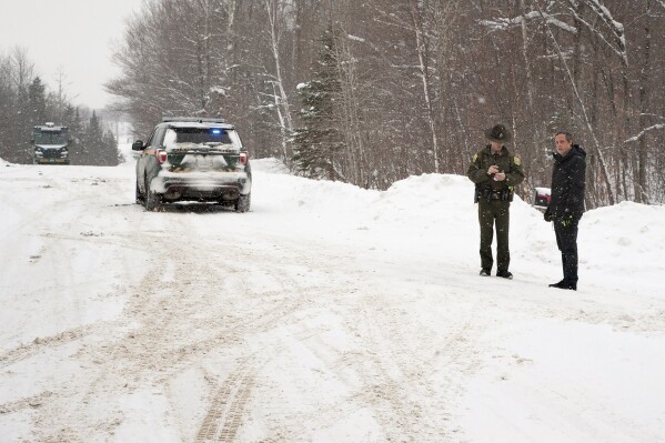 FILE - A Vermont state trooper, center, speaks to a homeowner, Jan. 8, 2018, near an area on Peacham Road in Barnet, Vt., where the body of Gregory Davis was found. One of the last of four men charged in an international murder-for-hire plot that led to the 2018 abduction and killing of a Vermont man pleaded guilty on Wednesday, March 13, 2024. (Dana Gray/Caledonian-Record via AP, File)