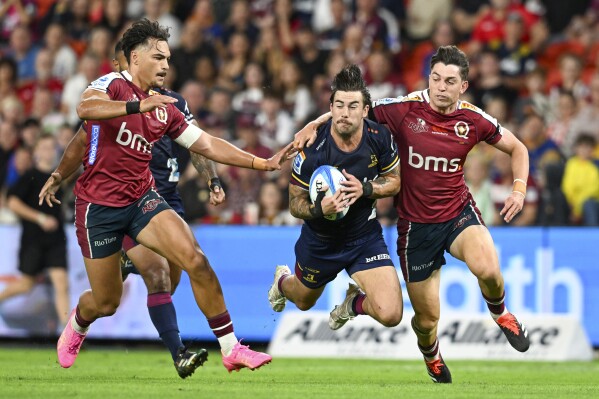 Connor Garden-Bachop, center, of the Highlanders is tackled by Jordan Petaia, left, and Jock Campbell of the Queensland Reds during their Super Rugby Pacific game at Suncorp Stadium in Brisbane, Australia, Friday, April 19, 2024. (Darren England/AAP Image via AP)