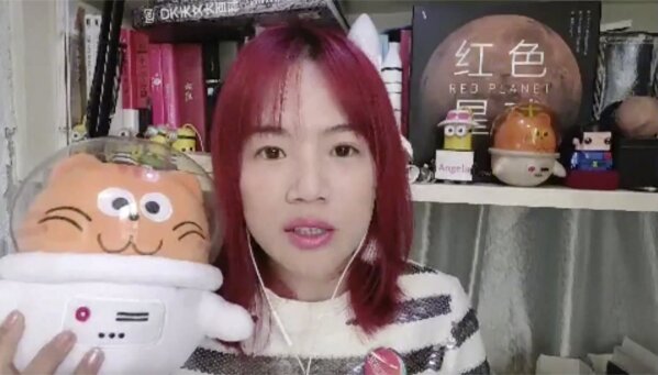 In this image taken from video, Cui Tingting, director of the China Mars Society, poses with some of the Mars-related items she has collected at her home in Shanghai, Wednesday, Feb. 10, 2021. China is falling in love with space, inspired by the ruling Communist Party's increasingly ambitious missions over the past two decades to fire humans into orbit and explore the moon and Mars. (AP Photo)