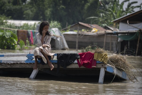 A flood victim sits on a submerged boat dock in Sandahkhaiti, a floating island village in the Brahmaputra River in Morigaon district, Assam, India, Wednesday, Aug. 30, 2023. (APPhoto/Anupam Nath)