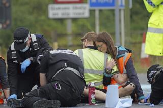 Police officers work to free protesters from Insulate Britain who had glued themselves to the highway, at a slip road at Junction 4 of the A1 motorway, near Hatfield, England, Monday, Sept. 20, 2021. Protesters are demonstrating for the government to insulate every home in Britain to tackle climate change and fuel poverty. (Steve Parsons/PA via AP)