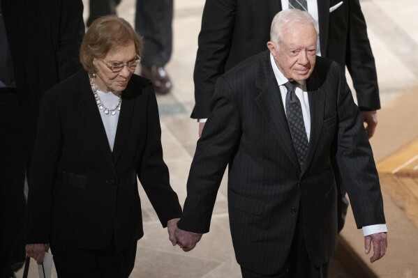 FILE - Former President Jimmy Carter, right, and his wife, former first lady Rosalynn Carter, hold hands as they walk from the state funeral of former President George H.W. Bush at the National Cathedral on December 5, 2018 in Washington.  The year Jimmy Carter first entered home hospice care, the 39th president celebrated his 99th birthday, paying tribute to his legacy and outliving his wife of 77 years.  Rosalynn Carter, who died in November 2023 after suffering from dementia, spent only a few days in hospice.  (AP Photo/Caroline Castor, File)