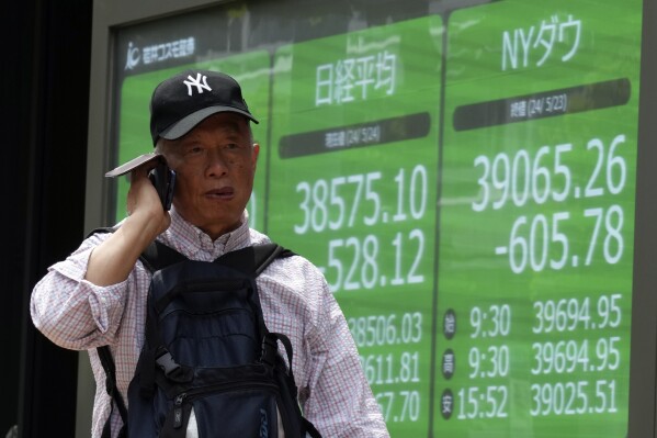 A person walks in front of an electronic stock board showing Japan's Nikkei and New York Dow indexes at a securities firm Friday, May 24, 2024, in Tokyo. (AP Photo/Eugene Hoshiko)
