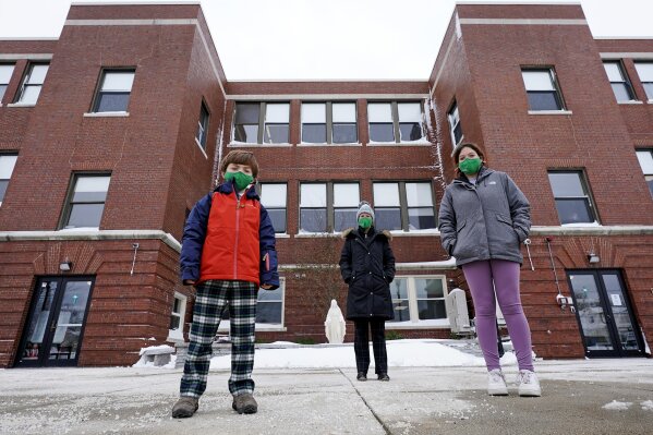 Head of School Jennifer Kowieski, center, poses with students Landon Freytag, of Newton, Mass., left, and Madeline Perry, of Brookline, Mass., right, outside the Saint Columbkille Partnership School, a Catholic school, Friday, Dec. 18, 2020, in the Brighton neighborhood of Boston. The families of both students decided to switch to the school, avoiding the challenges of remote learning at many public schools. (AP Photo/Charles Krupa)