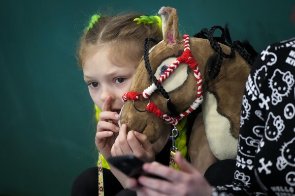 A girl watches races of their competitors during a Hobby horsing competition in St. Petersburg, Russia, on Sunday, April 21, 2024. Several dozen kids, 48 girls and one boy, from first-graders to teenagers gathered in a gymnasium in northern St. Petersburg, Russia's second largest city, for a hobby horsing competition. (AP Photo/Dmitri Lovetsky)