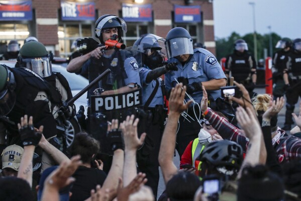 FILE - A police officer points a hand cannon at protesters who have been detained pending arrest on South Washington Street in Minneapolis, May 31, 2020, as protests continued following the death of George Floyd. At least 11 Minneapolis police officers were disciplined for alleged policy violations amid the unrest that followed the murder of George Floyd, with penalties ranging from firings to reprimands, newly released documents show Friday, April 5, 2024. (AP Photo/John Minchillo, File)