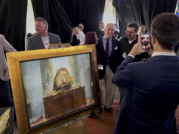 Roger Stone poses for photographs as a painting by Elisabeth Miller titled “Lion of Judah on the Resolute Desk” is displayed during the ReAwaken America Tour at Cornerstone Church in Batavia, N.Y., Friday, Aug. 12, 2022. While smaller in scale, the ReAwaken shows are similar in tone to the rallies former President Trump holds. Grievance and contempt for government institutions are regular themes. (AP Photo/Carolyn Kaster)