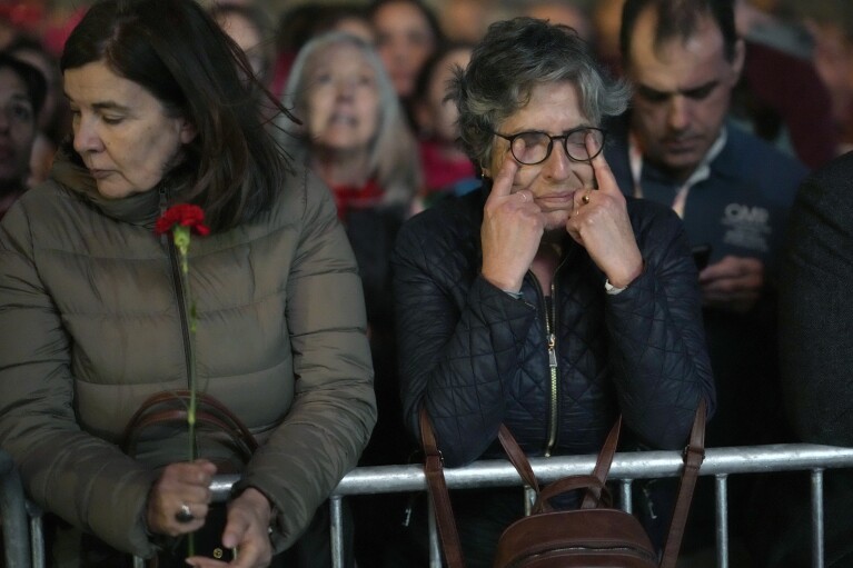 A woman wipes her tears while watching video clips about life in Portugal before 1974, at Lisbon's Comercio square, Wednesday, April 24, 2024, during a concert to celebrate the fiftieth anniversary of the Carnation Revolution. The April 25, 1974 revolution carried out by the army restored democracy in Portugal after 48 years of a fascist dictatorship. (AP Photo/Armando Franca)