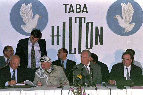 FILE - Palestinian team chief negotiator Ahmed Qreia "Abu Ala" initials the PLO-Israeli agreement while PLO Chairman Yasser Arafat, second left, Israeli Foreign Minister Shimon Peres, second right, and Israeli chief negotiator Uri Savir, right, who also initialed the agreement, look on at the Hilton hotel in Taba, Egypt on Sept. 24, 1995. Uri Savir, a prominent Israeli peace negotiator and dogged believer in the need for a settlement with the Palestinians, has died. He was 69. Israeli media said he died Friday, May 13, 2022. No cause of death was reported. Savir lead an Israeli delegation to negotiate a series of interim agreements with the Palestinians in 1993 that became known as the Oslo Accords. (AP Photo/Enric F.Marti, File)