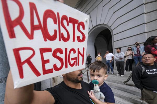 Shervin Aazami holding his son Barrett and a sign protest outside City Hall during the Los Angeles City Council meeting Tuesday, Oct. 11, 2022 in Los Angeles. (AP Photo/Ringo H.W. Chiu)
