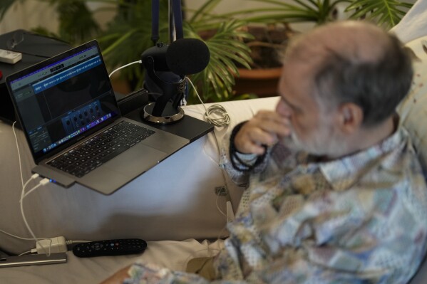 Michael Bommer, who is terminally ill with colon cancer, listens to his AI generated voice during a meeting with The Associated Press at his home in Berlin, Germany, Wednesday, May 22, 2024. Bommer, who has only a few more weeks to live, teamed up with friend who runs the AI-powered legacy platform Eternos to 