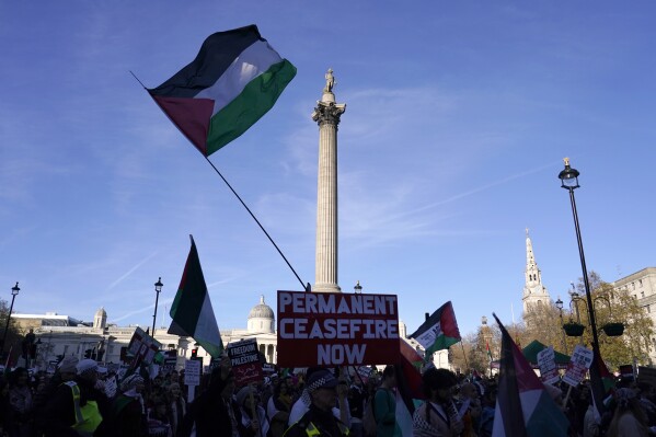 Protester hold flags and placards as they take part in a pro-Palestinian demonstration as pass by Trafalgar Square in London, Saturday, Nov. 25, 2023. (AP Photo/Alberto Pezzali)