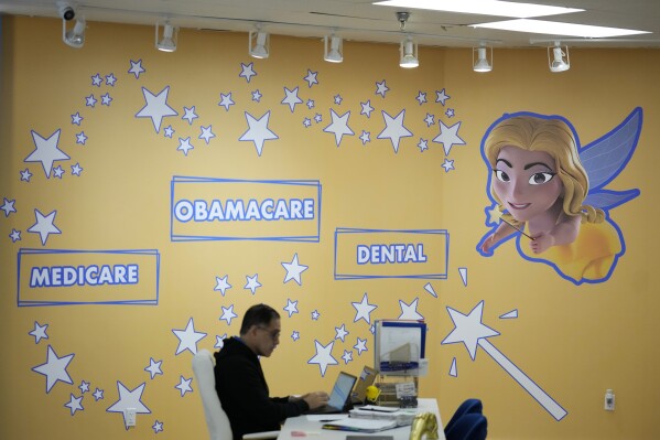 An employee works beside wall decorations depicting managing partner Odalys Arevalo as a fairy godmother, at Las Madrinas de los Seguros (Spanish for "The Godmothers of Insurance"), a health insurance agency serving Spanish-speaking clients, in their main location at a shopping center in Miami, Tuesday, Dec. 5, 2023. (AP Photo/Rebecca Blackwell)