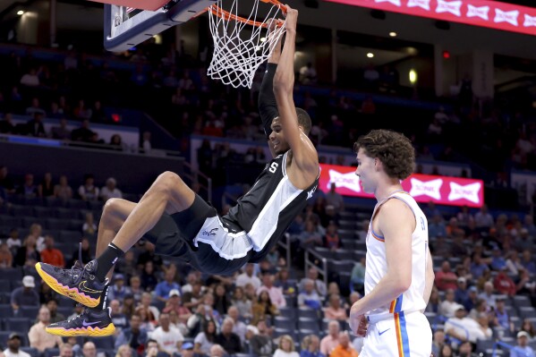 San Antonio Spurs center Victor Wembanyama, left, dunks next to Oklahoma City Thunder guard Josh Giddey, right, in the first half of a preseason NBA basketball game Monday, Oct. 9, 2023, in Oklahoma City. (AP Photo/Sarah Phipps)