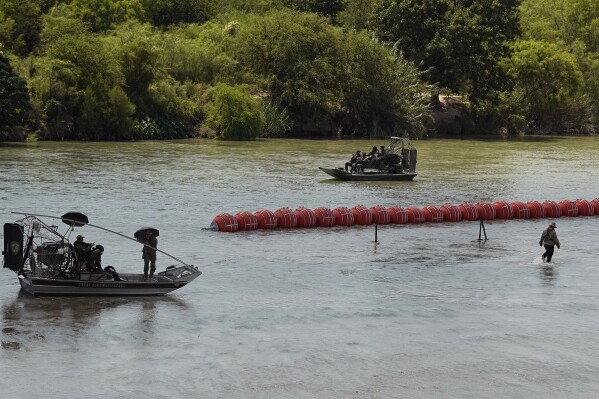 Texas State Troopers watch from an airboat as workers deploy a string of large buoys to be used as a border barrier at the center of the Rio Grande near Eagle Pass, Texas, Tuesday, July 11, 2023. The floating barrier is being deployed in an effort to block migrants from entering Texas from Mexico. (AP Photo/Eric Gay)