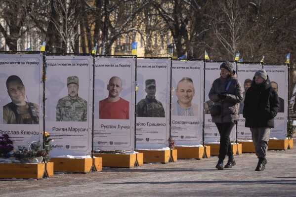 Women walk next to photos of city residents who joined the Ukrainian army and were killed battling Russia, at a memorial to fallen soldiers in Chernihiv, Ukraine, Sunday, Feb. 16, 2025. (AP Photo/Efrem Lukatsky)