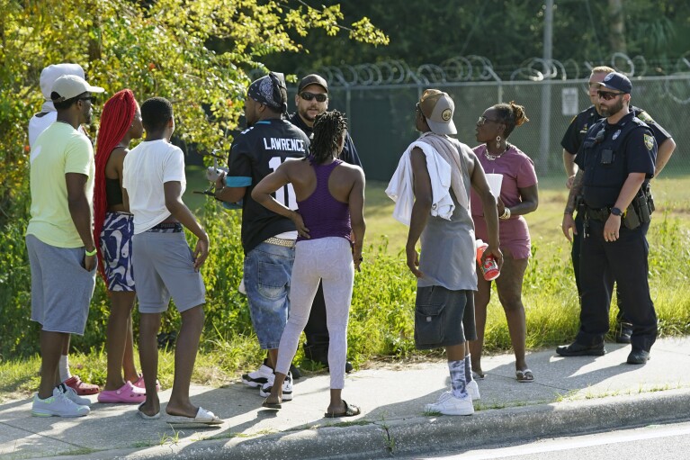 Residents talk with Jacksonville police officers near the scene of a mass shooting at a Dollar General store, Saturday, Aug. 26, 2023, in Jacksonville, Fla. (AP Photo/John Raoux)