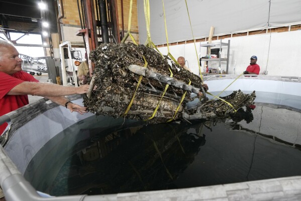 Wayne Lusardi, Michigan's state maritime archaeologist with the Department of Natural Resources helps guide the 1,200-pound mussel-encrusted engine from a P-39 World War II-era fighter plane flown by a member of the famed Tuskegee airmen into a chemical solution, Thursday, Aug. 17, 2023 at the Tuskegee Airmen National Historical Museum in Detroit. The plane was flown by a member of the famed Tuskegee airmen that crashed during training nearly 80 years ago near Port Huron, about 60 miles northeast of Detroit. (AP Photo/Carlos Osorio)