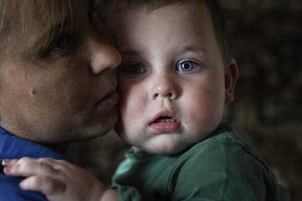Olga Bezborodova calms her 20-month-old son, Mykola, in her home, which has no electricity, in the village of Rubizhne, Kharkiv region, Ukraine, on Wednesday, April 17, 2024. (AP Photo/Evgeniy Maloletka)