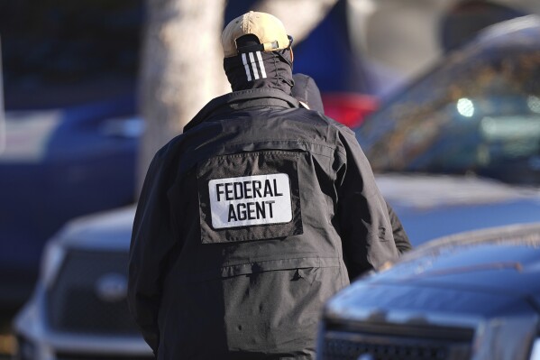 A member of law enforcement stand near an entrance to an apartment complex during a raid by federal agents Feb. 5, 2025, in east Denver. (AP Photo/David Zalubowski, File)