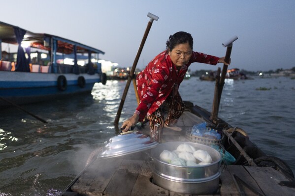 Nguyen Thi Thuy, a vendor who sells steamed buns on a floating market, lifts the lid of her steamer to attract tourists in Can Tho, Vietnam, Wednesday, Jan. 17, 2024. (AP Photo/Jae C. Hong)