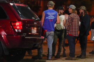 A group holds rifles as they watch protesters on the street Tuesday, Aug. 25, 2020, in Kenosha, Wis. Protests continued following the police shooting of Jacob Blake two days earlier. (AP Photo/Morry Gash)