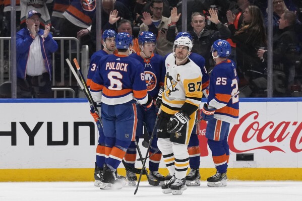Pittsburgh Penguins center Sidney Crosby (87) looks up at the scoreboard as the New York Islanders celebrate a goal by Simon Holmstrom, third from left, during the third period of an NHL hockey game Wednesday, April 17, 2024, in Elmont, N.Y. (AP Photo/Seth Wenig)