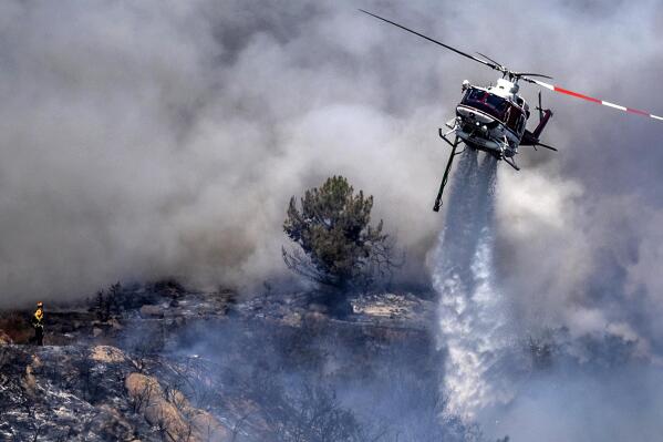 A firefighter is dwarfed by an aerial drop at the the Chaparral Fire in Murrieta which still blazes, Sunday, August 29, 2021. Several homes appear to be evacuated in the area. (Cindy Yamanaka/The Orange County Register via AP)