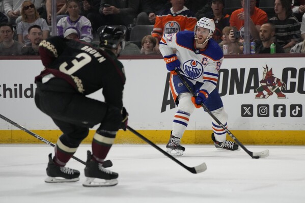 Edmonton Oilers center Connor McDavid looks to pass in front of Arizona Coyotes defenseman Josh Brown in the first period during an NHL hockey game, Monday, Feb. 19, 2024, in Tempe, Ariz. (AP Photo/Rick Scuteri)
