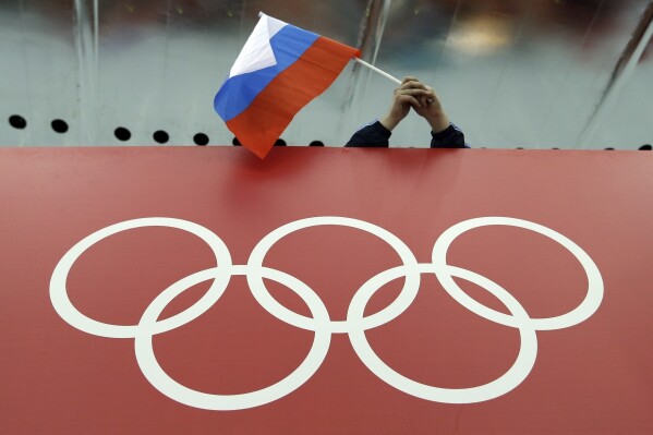 FILE - A Russian flag is held above the Olympic Rings at Adler Arena Skating Center during the Winter Olympics in Sochi, Russia on Feb. 18, 2014. Some Russian athletes will be allowed to compete at the 2024 Paris Olympics, the IOC said Friday, Dec. 8, 2023 in a decision that removed the option of a blanket ban over the invasion of Ukraine. (AP Photo/David J. Phillip, File)