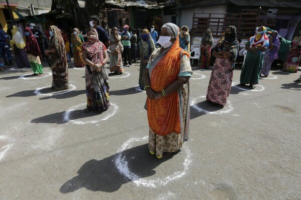 FILE- In this April 11, 2020 file photo, Indian women stand in marked circles to maintain distance as they wait to receive face masks, gloves and hand sanitizers distributed by the Rapid Action Force (RAF) during lockdown to control the spread of the new coronavirus in Ahmedabad, India. India, a bustling country of 1.3 billion people, has slowed to an uncharacteristic crawl, transforming ordinary scenes of daily life into a surreal landscape. The country is now under what has been described as the world’s biggest lockdown, aimed at keeping the coronavirus from spreading and overwhelming the country’s enfeebled health care system. (AP Photo/Ajit Solanki, File)