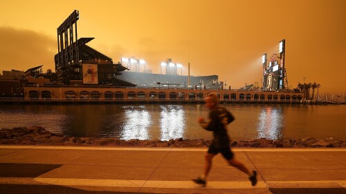 FILE - A jogger runs along McCovey Cove outside Oracle Park in San Francisco on Sept. 9, 2020, under dark skies from wildfire smoke.  As Earth's climate continues to change from heat-trapping gases emitted into the air, fewer people are going outside.  Scientists say wildfire smoke can reach from rising and deadly fingers.  (AP Photo/Tony Avelar, File)