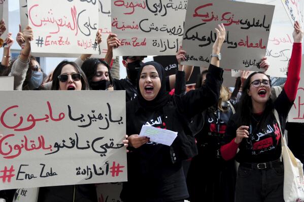 A woman holds a poster reading "I can use the law against him" , left, during a protest outside the court house in Nabeul, Tunisia, Thursday, Oct.28, 2021. A group of Tunisian feminist activists held a small protest outside a courthouse in Nabeul, Tunisia,to mark the beginning of a controversial case in which an MP is facing charges of sexual harassment and public indecency. In 2019, a school girl posted photos on social media of Qalb Tounes MP Zouhair Makhlouf allegedly performing a sexual act in his car outside her high school. (AP Photo/Hassene Dridi)