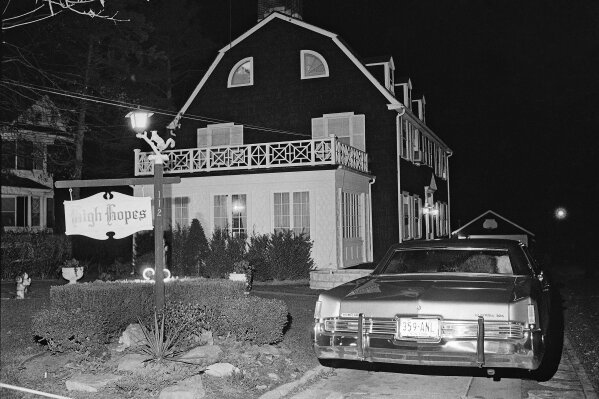 FILE - In this Nov. 14, 1974 file photo, police and members of the Suffolk County Coroner's Office investigate the murder of six people found shot in Amityville, N.Y. Ronald DeFeo, Jr., the man convicted of slaughtering his parents and four siblings in a home that later inspired the book and movie "The Amityville Horror"  died Friday, March 12, 2021 at Albany Medical Center,  where he was taken Feb. 2 from a prison in New York’s Catskill Mountains, prison officials said Monday, March 15. He was 69. (AP Photo/Richard Drew, File)