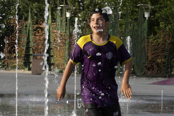 A boy enjoys a water fountain at the Ebrahim Park while temperature reaches 38 C (100.4 F) in Tehran, Iran, Tuesday, Aug. 1, 2023. Iran announced a nationwide two-day, Wednesday and Thursday, holiday because of increasing temperatures. (AP Photo/Vahid Salemi)