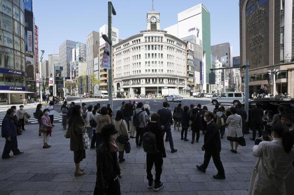 FILE - People wearing face masks to help curb the spread of the coronavirus wait at pedestrian crossings in Tokyo on March 26, 2021. The Bank of Japan made its offer for unlimited bond purchases Monday, Feb. 14, 2022, a move aimed at curbing the surge of long-term interest rates. (AP Photo/Eugene Hoshiko, File)