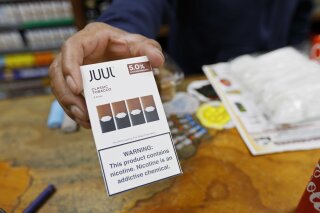 File - In this June 17, 2019, file photo, a cashier displays a packet of tobacco-flavored Juul pods at a store in San Francisco. Investigators from 39 states will look into the marketing and sales of vaping products by Juul Labs, including whether the company targeted youths and made misleading claims about nicotine content in its devices, officials announced Tuesday, Feb. 25, 2020. Juul released a statement saying it has halted television, print and digital advertising and eliminated most flavors in response to concerns by government officials and others.  (AP Photo/Samantha Maldonado, File)