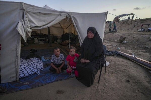 A Palestinian woman sits in front of her makeshift tent with her grandchildren after been displaced by the Israeli air and ground offensive on the Gaza Strip at a camp in Deir al Balah, Monday, May 13, 2024. Palestinians on Wednesday, May 15, 2024, will mark the 76th year of their mass expulsion from what is now Israel. It's an event that is at the core of their national struggle, but in many ways pales in comparison to the calamity now unfolding in Gaza. (AP Photo/Abdel Kareem Hana)