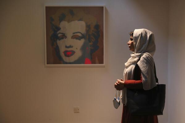 Fatemeh Rezaei, a retired teacher, stands next to Marilyn Monroe portrait by American artist Andy Warhol at Tehran Museum of Contemporary Art in Tehran, Iran, on Tuesday, Oct. 19, 2021. Iranians are flocking to Tehran's contemporary art museum to marvel at American pop artist Andy Warhol’s iconic work. (AP Photo/Vahid Salemi)