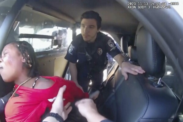 This image made from video provided by the Charlotte-Mecklenburg, N.C., Police Department shows officers attempting to put a woman in the back of a police car after arresting her. On Tuesday, Dec. 12, 2023, police released the video from the arrest in North Carolina last month, showing that before an officer repeatedly punched a Black woman while others held her down, the woman struck an officer in the face and he responded by hitting her back and knocking her off her feet. (Charlotte-Mecklenburg Police Department via AP)