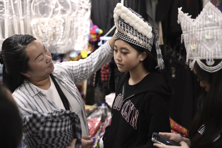 Alesia Lor tries on traditional Hmong New Year headwear with family members at a stall in the Hmong Village covered market in St. Paul, Minn., on Thursday, Nov. 16, 2023. For the New Year celebrations held in the fall, the Hmong, Southeast Asian refugees who settled in the United States after fighting on its side in the Vietnam War, traditionally buy or make new clothes in addition to holding spiritual ceremonies. (AP Photo/Mark Vancleave)